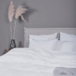 grijze muur met beige bed, roze plant en wit dekbedovertrek