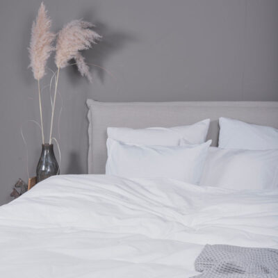 grijze muur met beige bed, roze plant en wit dekbedovertrek