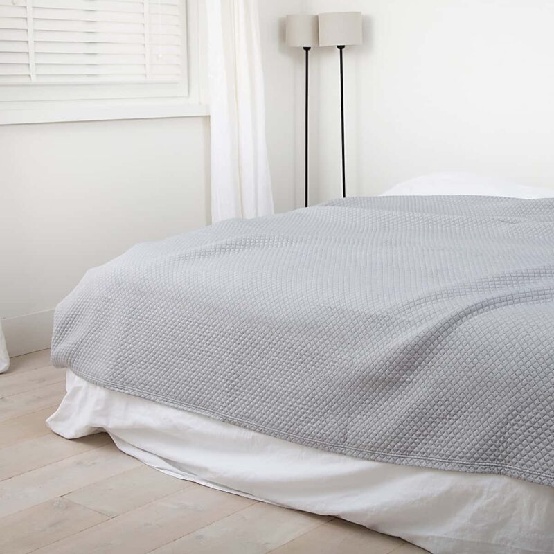 slaapkamer met houten vloer en luxe grijze bedsprei in ruitjes