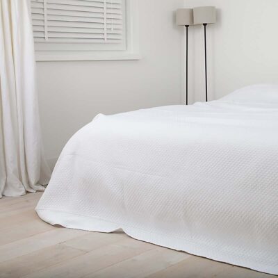 slaapkamer met wit, gordijnen, lamp en houten vloer. Bedsprei op bed is wit van kleur
