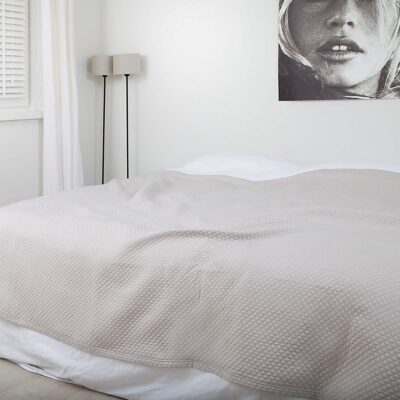 slaapkamer met schilderij, houten vloer en luxe zand kleurige bedsprei in ruitjes