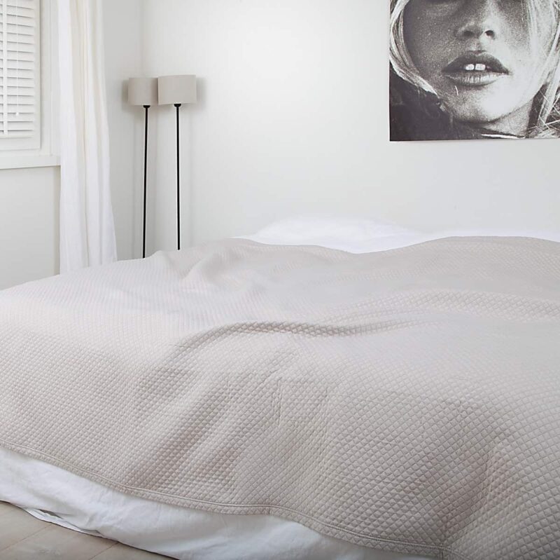 slaapkamer met schilderij, houten vloer en luxe zand kleurige bedsprei in ruitjes