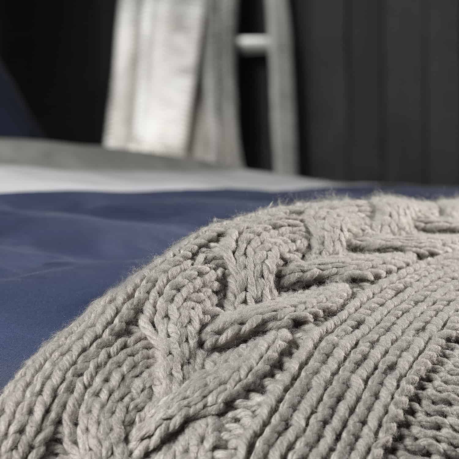 grijze plaid en stuk van een bed van dichtbij