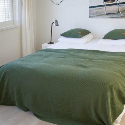 bed in slaapkamer met wit dekbed en groene wafel sprei