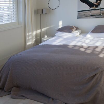 slaapkamer met een bed en lichte muren, grijze wafel sprei op het bed