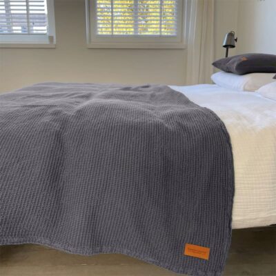 slaapkamer met een bed en lichte muren, grijze wafel sprei op het bed