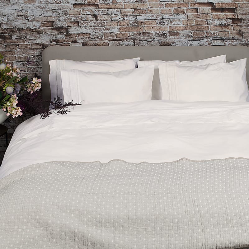 steen muur bij slaapkamer met bed en broderie dekbedovertrek in offwhite