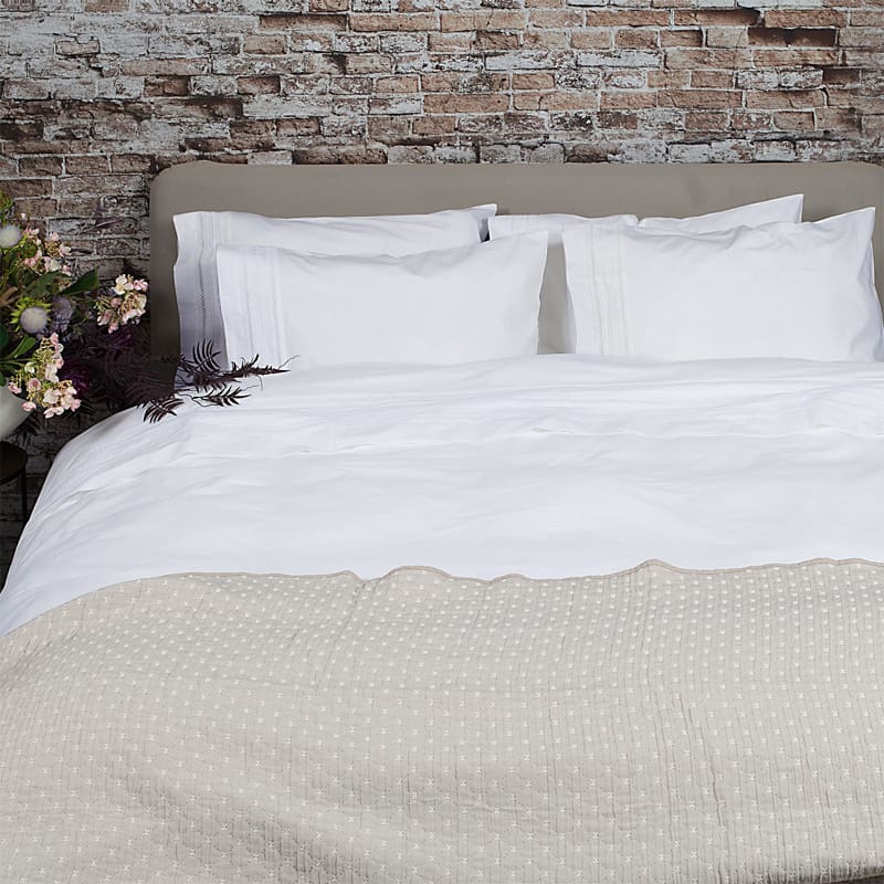 stenen muur met bed en wit broderie dekbedovertrek