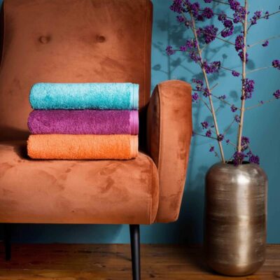 roest gekleurde suède fauteuil met vaas en luxe handdoeken in oranje, roze en blauw