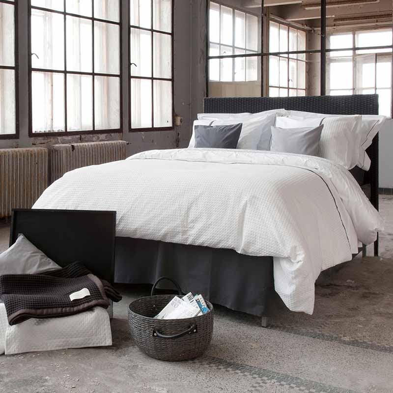 bed in industriële kamer met wit wafelstof dekbedovertrek