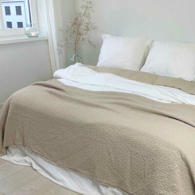bed met beige bedsprei en witte kussens