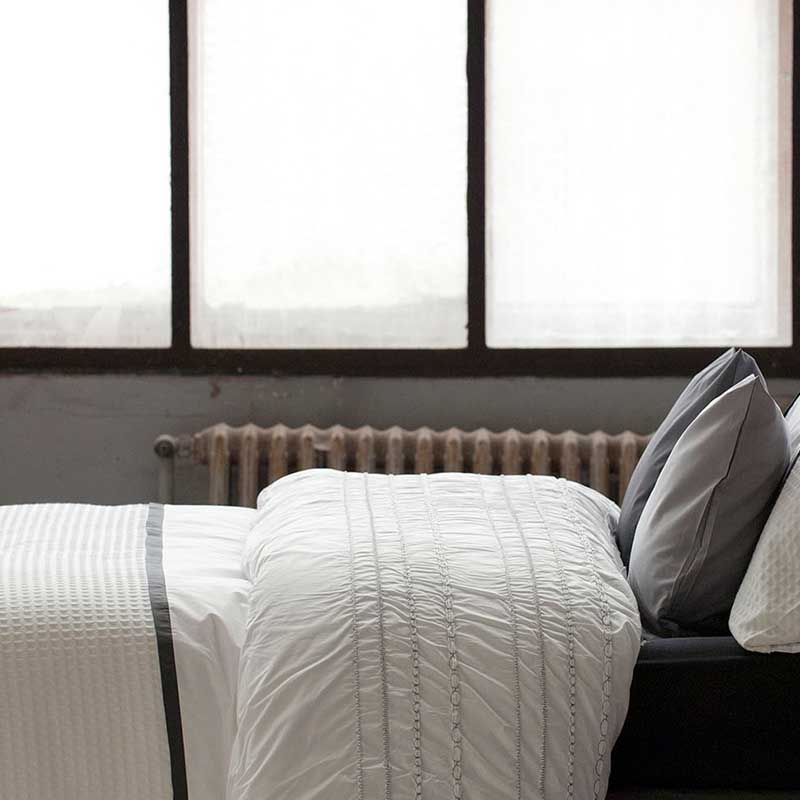 zijkant bed met wit/ grijs beddengoed