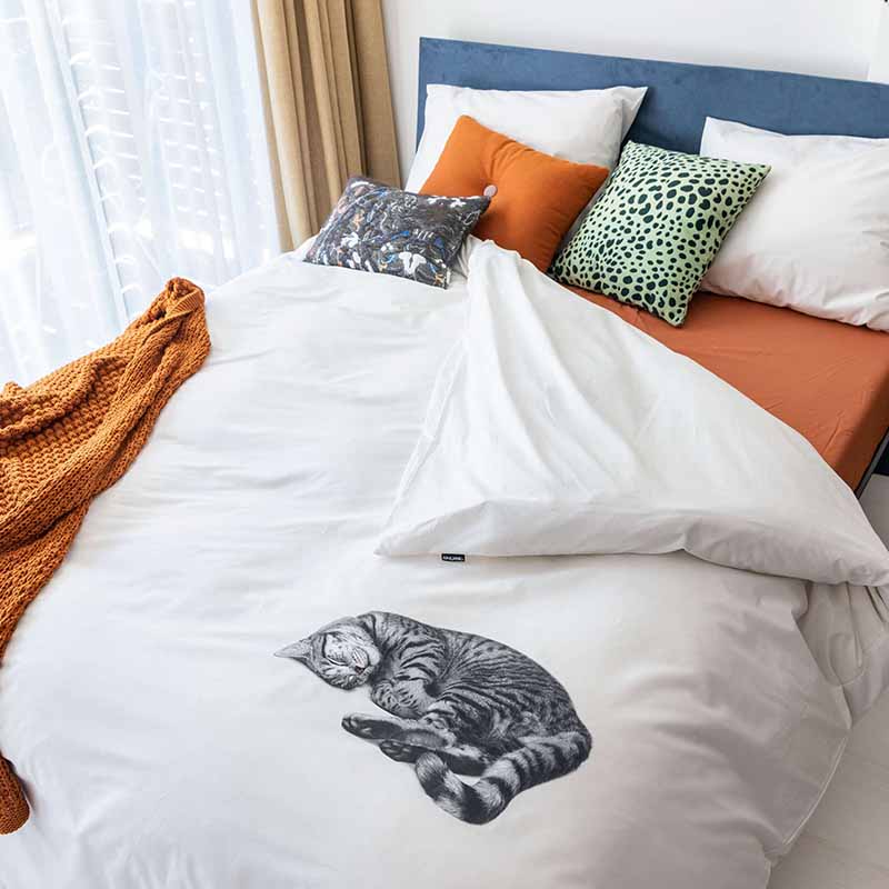 bed met kussens en wit dekbedovertrek van flanel met poes motief erop