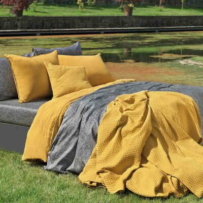 bed op gras met gele kussens, bedsprei en luxe lakens