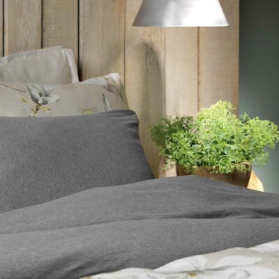 bed van zijkant met grijze bovenlakens en kussens