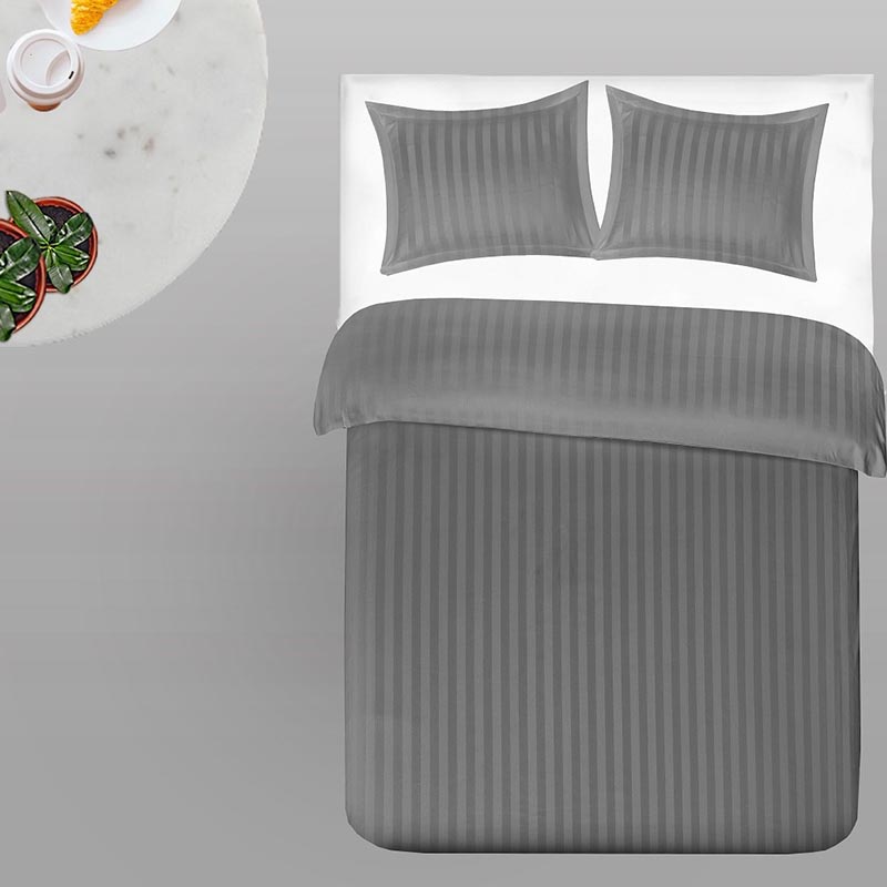 betonlook vloer, bed met twee kussens en grijs dekbedovertrek met een rond tafeltje ernaast