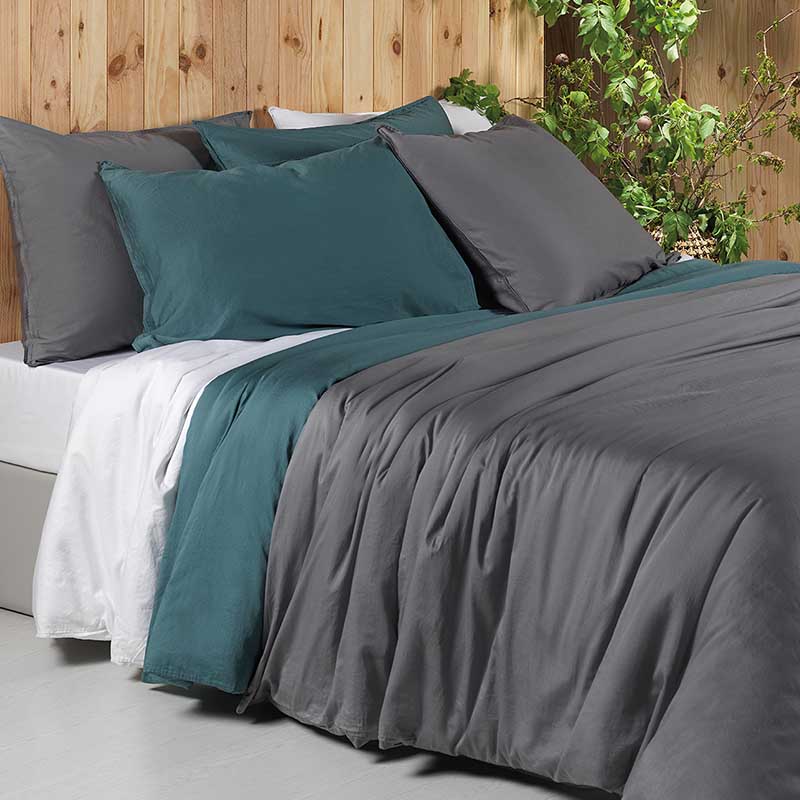 bed met houten wand, plant en 3 dekbedden in groen, grijs en wit