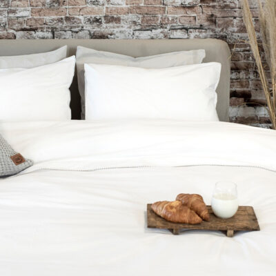 bed met wit dekbedovertrek en stenen muur