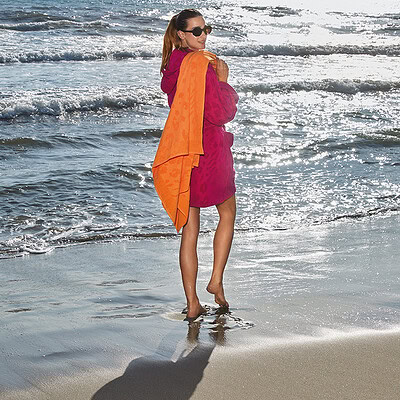 vrouw op strand in fel gekleurde dames badjas met strandlaken
